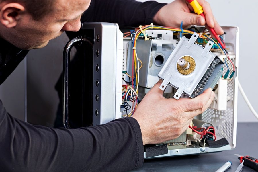 Serviceman electrician repairs a magnetron in the microwave. The man repairs the microwave. Replacing the magnetrons in the microwave.