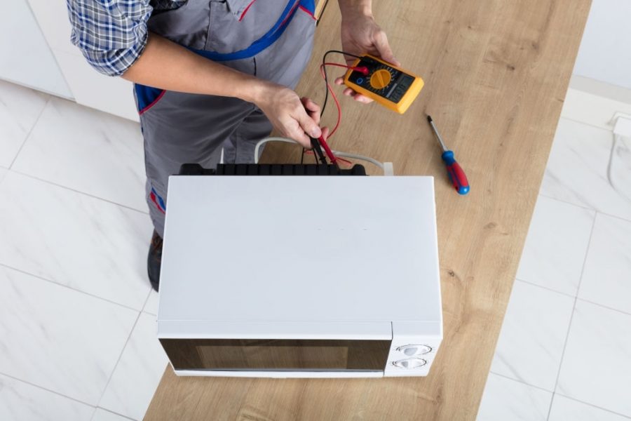 Male Technician Checking Microwave Using Digital Multimeter